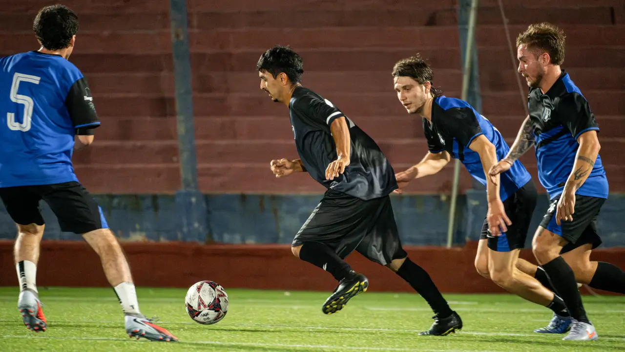 Jugador acelerando con la pelota rodeado de rivales en partido nocturno