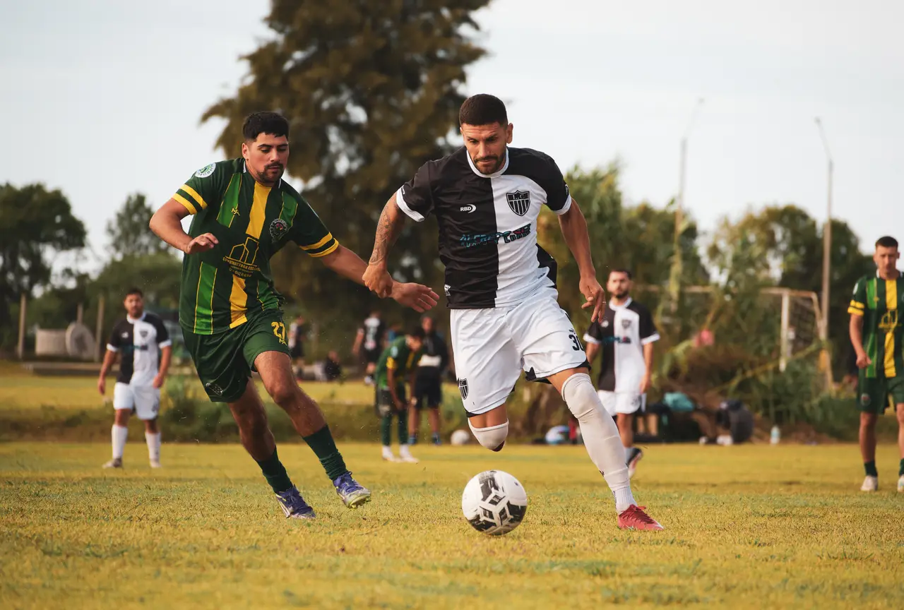 Jugador avanzando con la pelota contra rival de camiseta verde