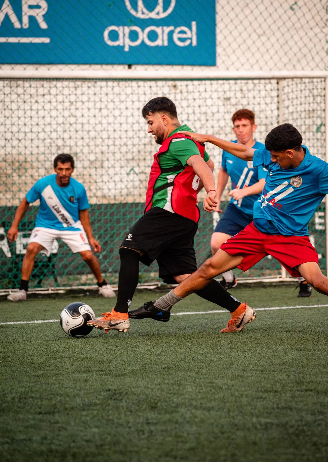 Jugador de camiseta roja y verde avanzando con la pelota ante rivales celestes